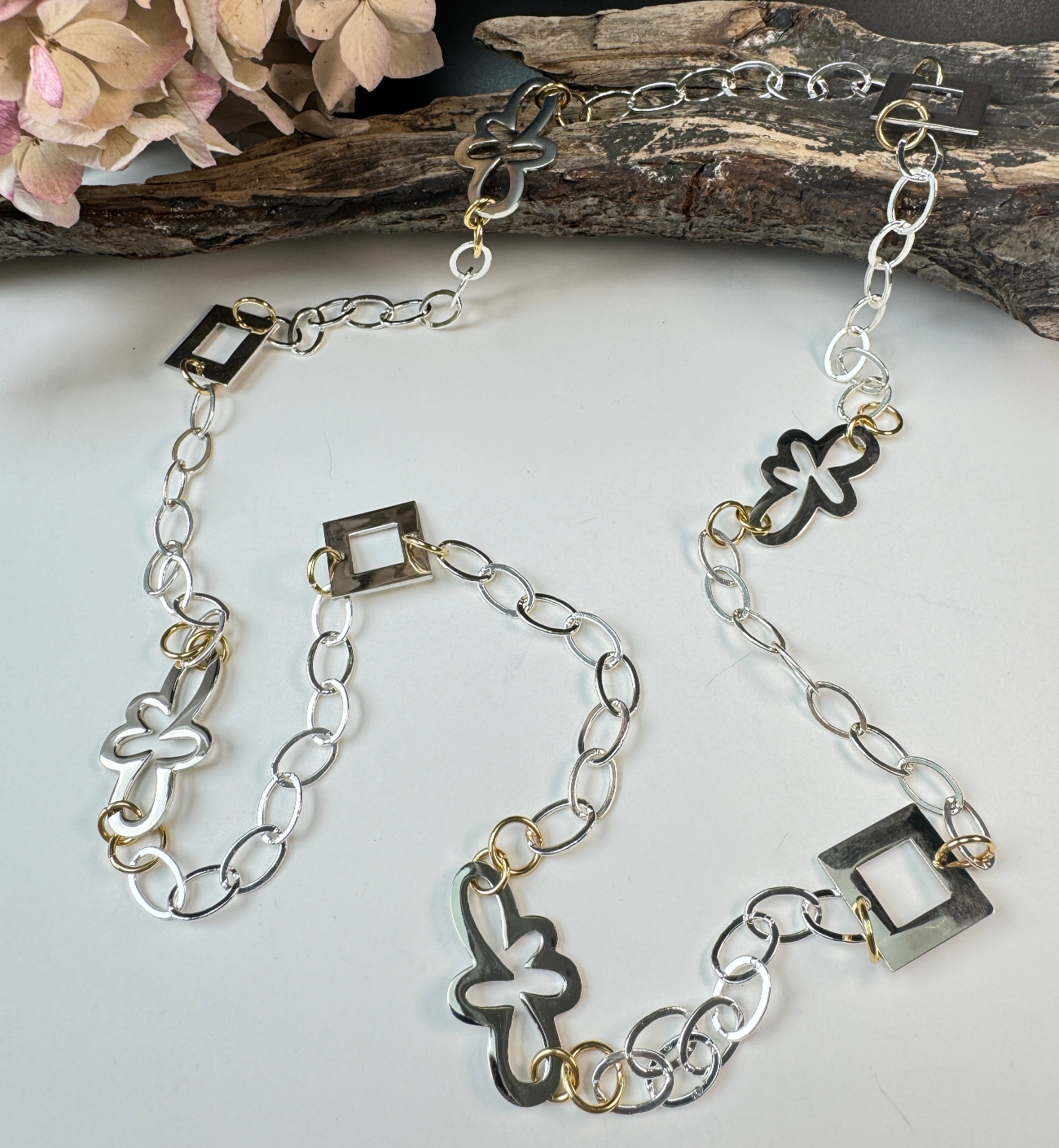 Långt handgjort halsband med egendesignade fyrkanter och blommor, silverpläterad mässingskedja och detaljer i 18K guld PVD. Bär på flera sätt. Design by Brandeby