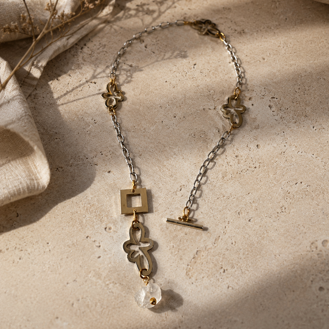 Kort halsband med äkta rå bergkristall, egendesignade blommor i rostfritt stål med sterling silver-pläterade detaljer och gulddetaljer med 18K guld PVD-beläggning. Texturerad kedja och handgjord design från Design by Brandeby.