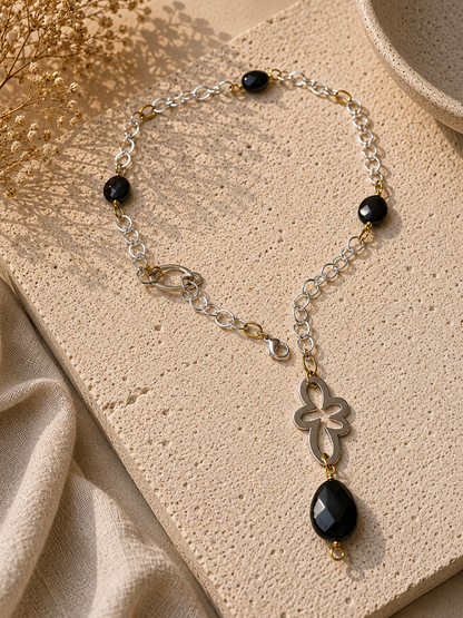 Långt halsband med fasettslipad svart onyx, paperclip-kedja och egendesignade detaljer i rostfritt stål med sterling silver-pläterade detaljer. Guldringar med 18K guld PVD-beläggning och flexibel längd. Design by Brandeby.