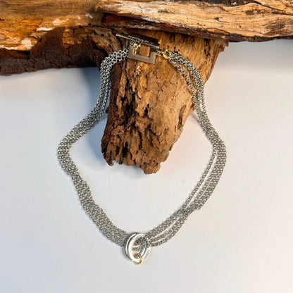 Circle Of Life Halsband i sterlingsilver från Design by Brandeby, med sammankopplade ringar och ett unikt spänne, visas elegant på naturligt trä.