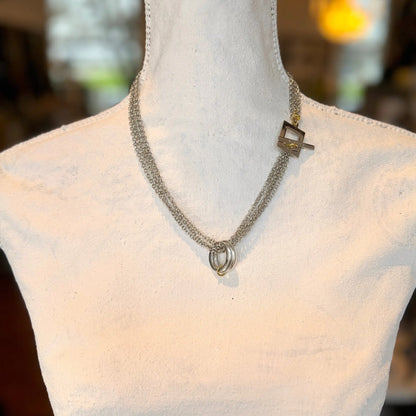 En skyltdocka visar upp det tvålagrade Circle Of Life Halsband av Design by Brandeby, med en kedja med sammankopplade ringar och en annan med en geometrisk kubberlock. Den mjukt suddiga bakgrunden accentuerar dess fantastiska design.