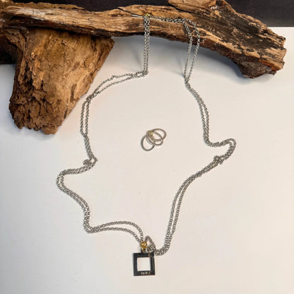 Sterling silver kedjor från Design by Brandeby's Circle Of Life Halsband skapar en personform på en vit bakgrund. Tre ringar fungerar som ögon och mun, med trä som tyder på hår. Ett fyrkantigt hänge inskrivet "RIP" hänger dystert från kedjan.
