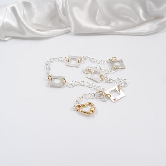 kort silver halsband med fyrkanter guld detaljer och handgjord kedja med ett guld hjärta som lås design by brandeby