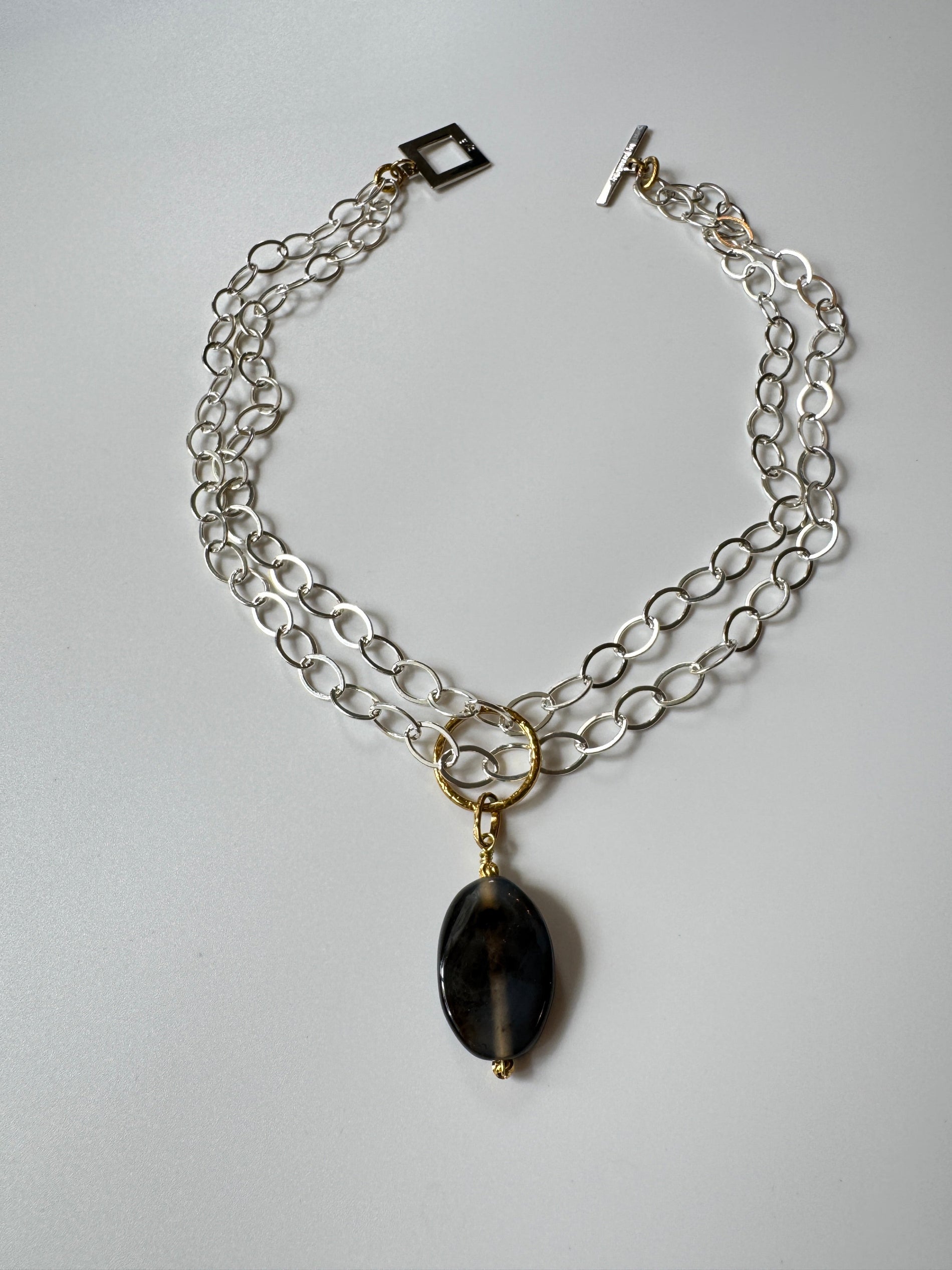 Elegant hänge med äkta svart agat och tunn guldring i rostfritt stål med 18K PVD-plätering. Ett stilrent och tidlöst smycke som passar både vardag och fest. Handgjort av Design by Brandeby.