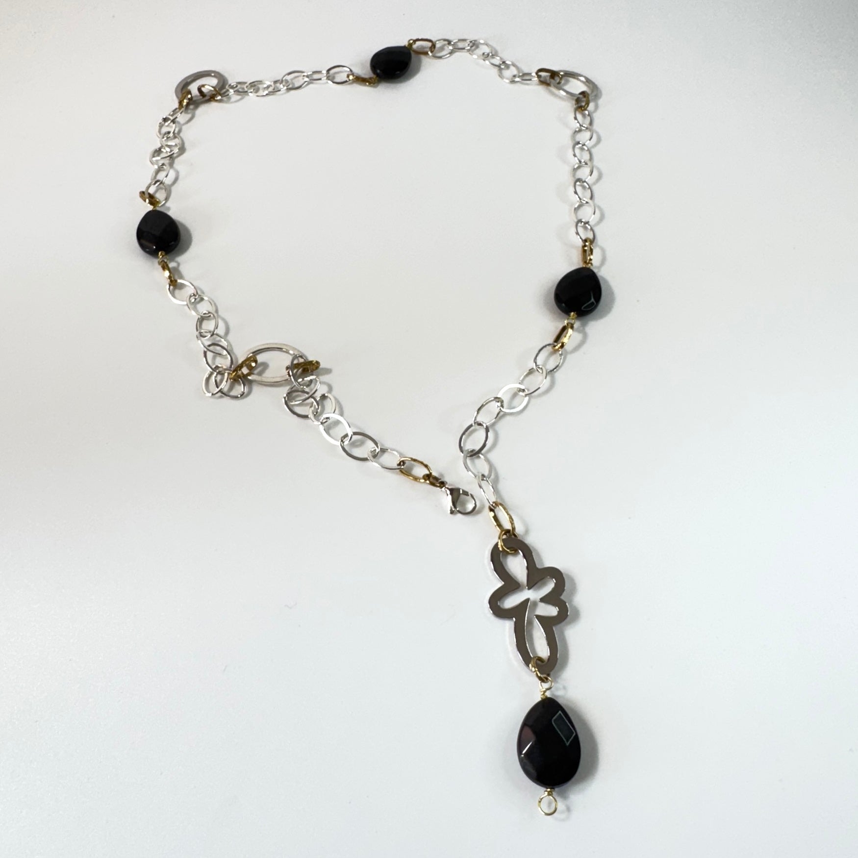 Långt halsband med fasettslipad svart onyx, paperclip-kedja och egendesignade detaljer i rostfritt stål med sterling silver-pläterade detaljer. Guldringar med 18K guld PVD-beläggning och flexibel längd. Design by Brandeby.