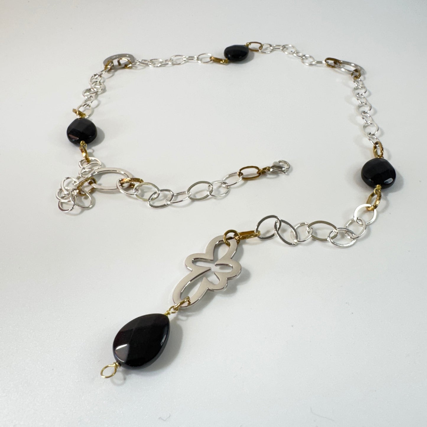 Långt halsband med fasettslipad svart onyx, paperclip-kedja och egendesignade detaljer i rostfritt stål med sterling silver-pläterade detaljer. Guldringar med 18K guld PVD-beläggning och flexibel längd. Design by Brandeby.