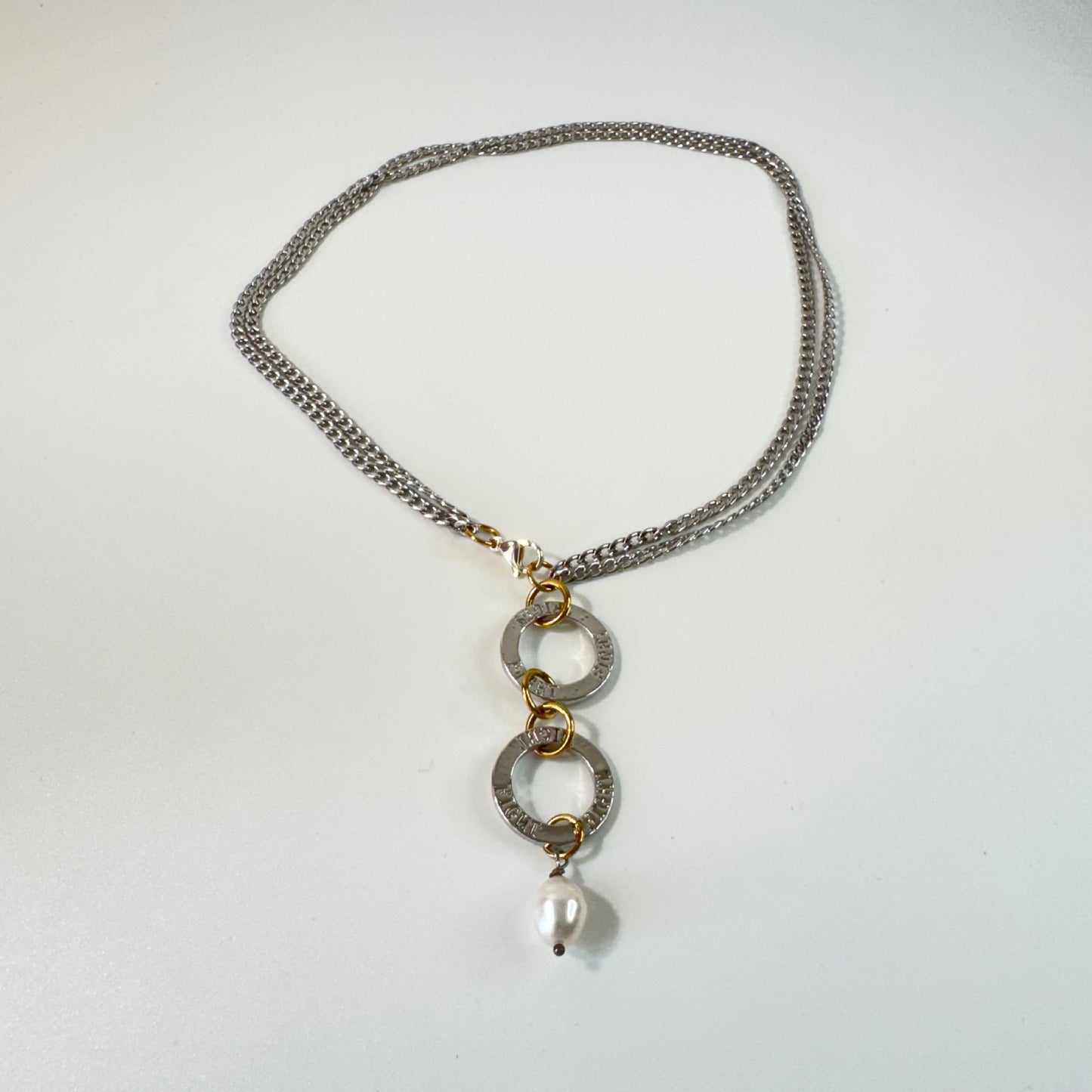 Flexibelt halsband med två cirklar med texten Fight, äkta vit sötvattenspärla och gulddetaljer i 18K PVD. Bär det kort eller långt för olika uttryck. Handgjort av Design by Brandeby.