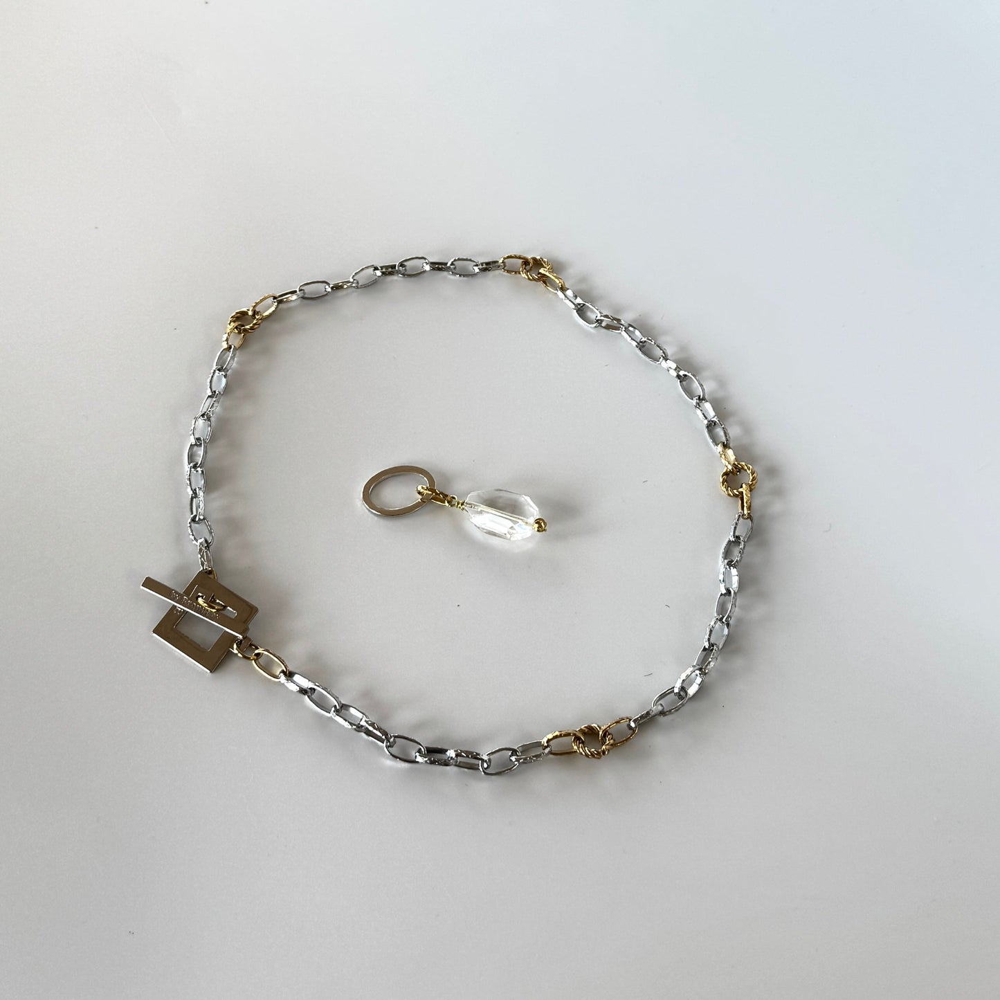 Elegant hänge med äkta bergkristall, fasade kanter och egendesignad cirkel i rostfritt stål med sterling silver-pläterade detaljer. Gulddetaljer i rostfritt stål med 18K guld PVD-beläggning. Handgjort av Design by Brandeby.