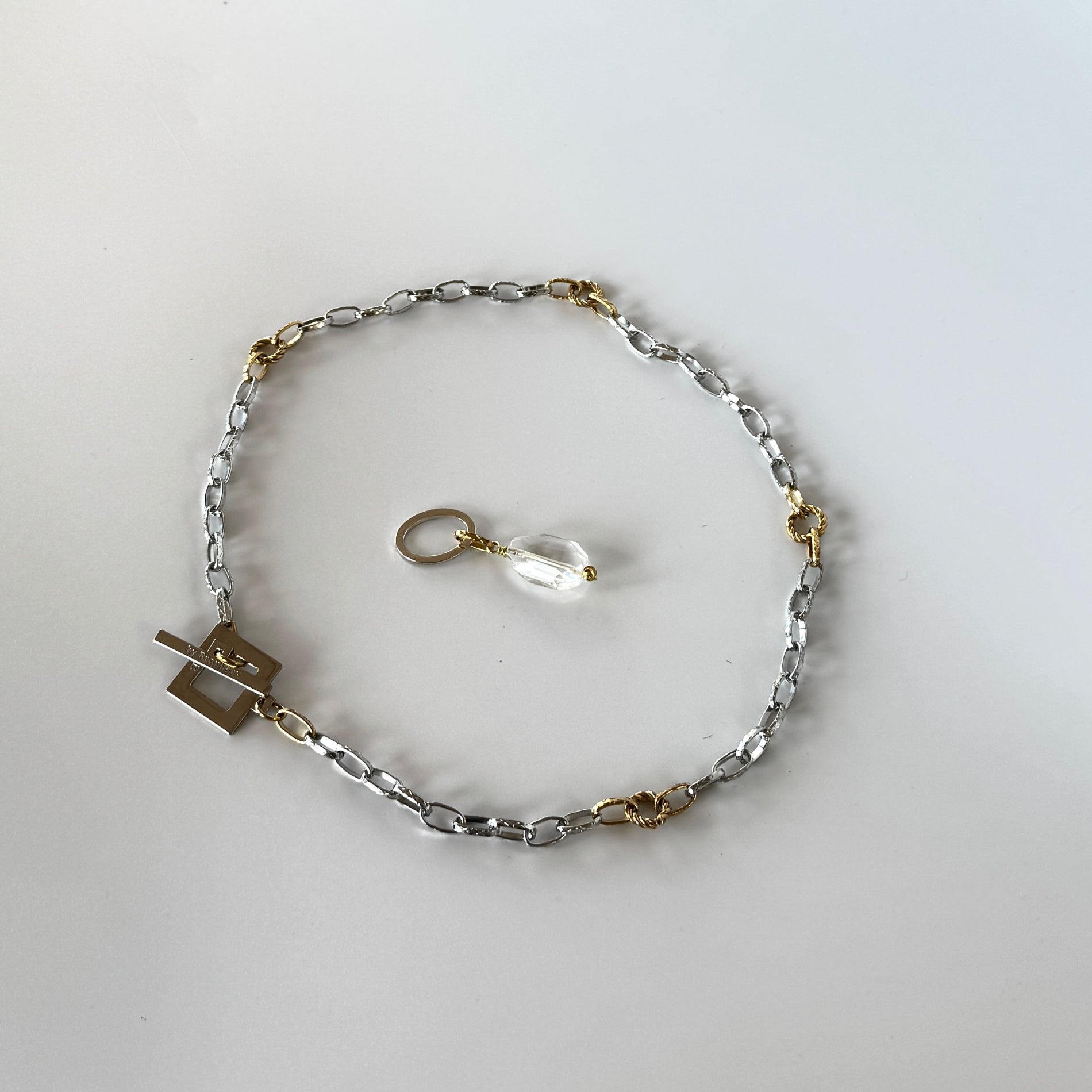 Elegant hänge med äkta bergkristall, fasade kanter och egendesignad cirkel i rostfritt stål med sterling silver-pläterade detaljer. Gulddetaljer i rostfritt stål med 18K guld PVD-beläggning. Handgjort av Design by Brandeby.