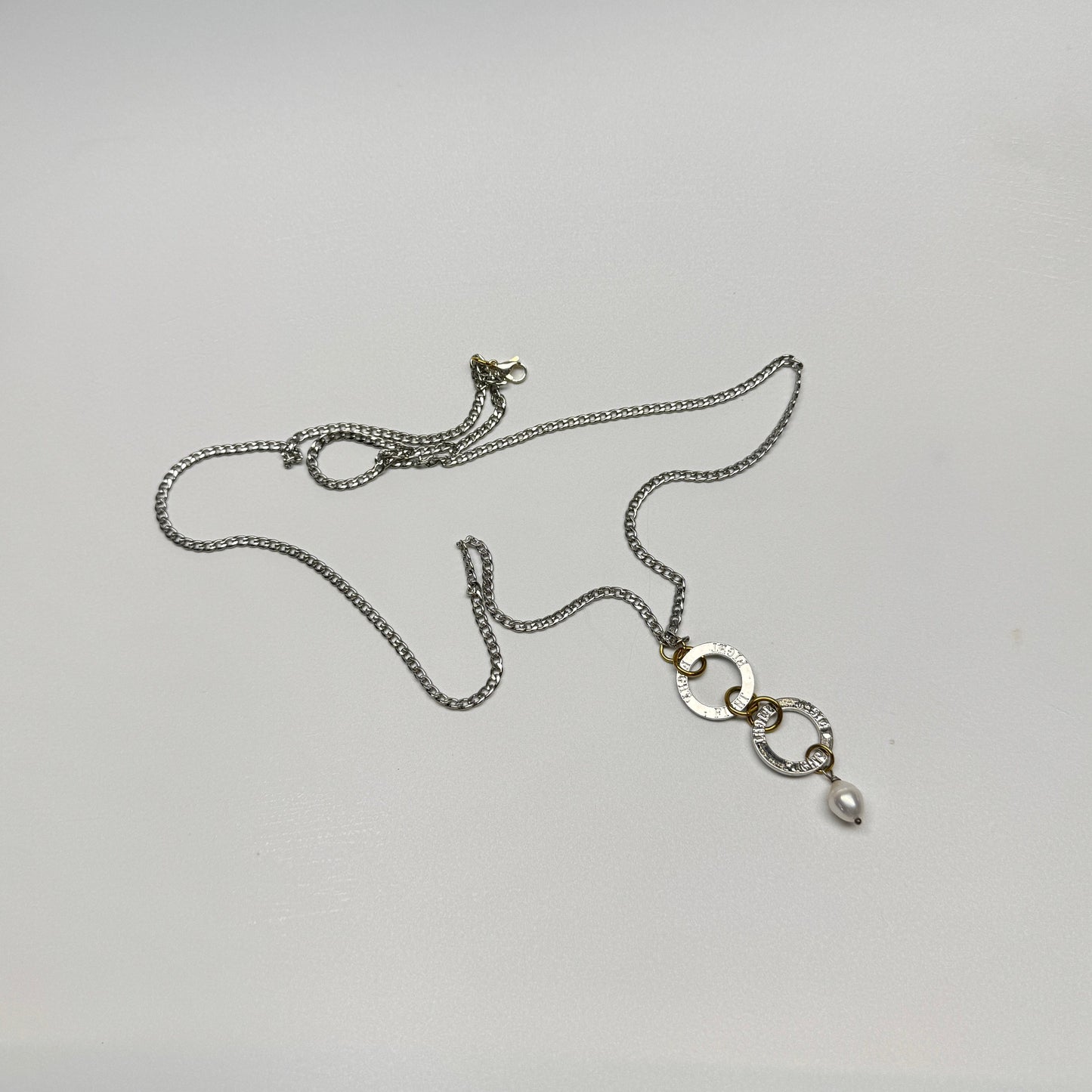 Flexibelt halsband med två cirklar med texten Fight, äkta vit sötvattenspärla och gulddetaljer i 18K PVD. Bär det kort eller långt för olika uttryck. Handgjort av Design by Brandeby.