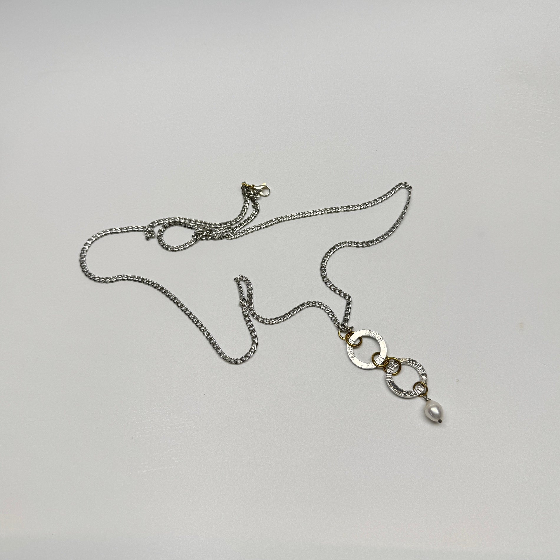 Flexibelt halsband med två cirklar med texten Fight, äkta vit sötvattenspärla och gulddetaljer i 18K PVD. Bär det kort eller långt för olika uttryck. Handgjort av Design by Brandeby.