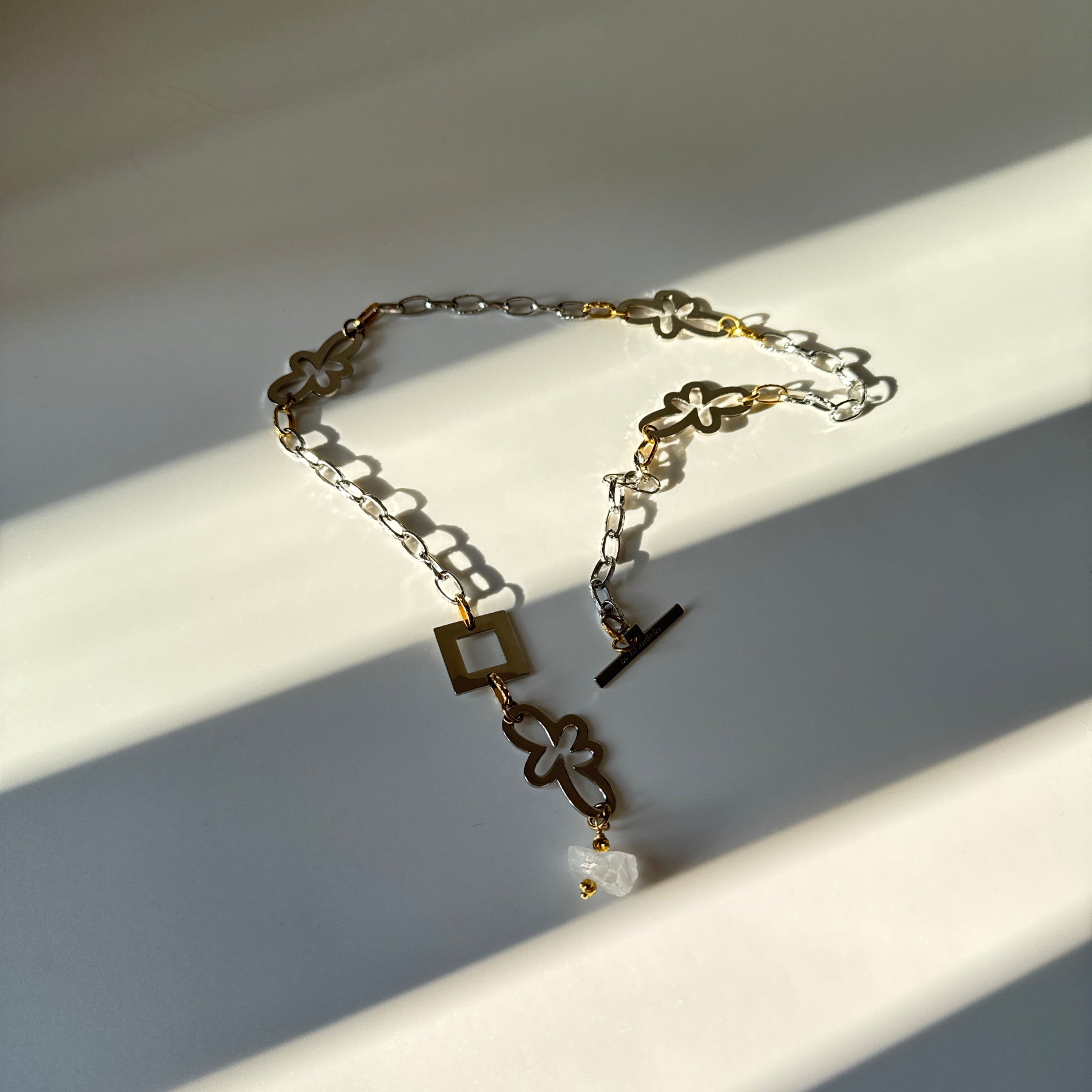 Halsband med äkta rå bergkristall, silverfärgad kedja, egendesignade blommor och guldringar i 18K PVD. Handgjort i rostfritt stål med sterling silver-pläterade detaljer. Ett unikt statementhalsband från Design by Brandeby.