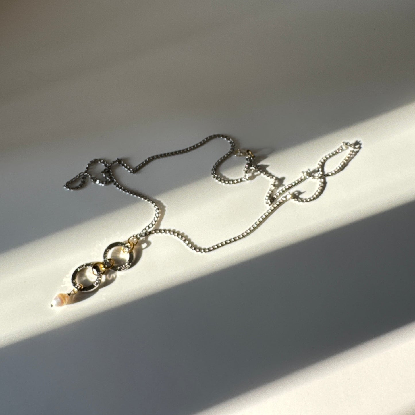 Flexibelt halsband med två cirklar med texten Fight, äkta vit sötvattenspärla och gulddetaljer i 18K PVD. Bär det kort eller långt för olika uttryck. Handgjort av Design by Brandeby.