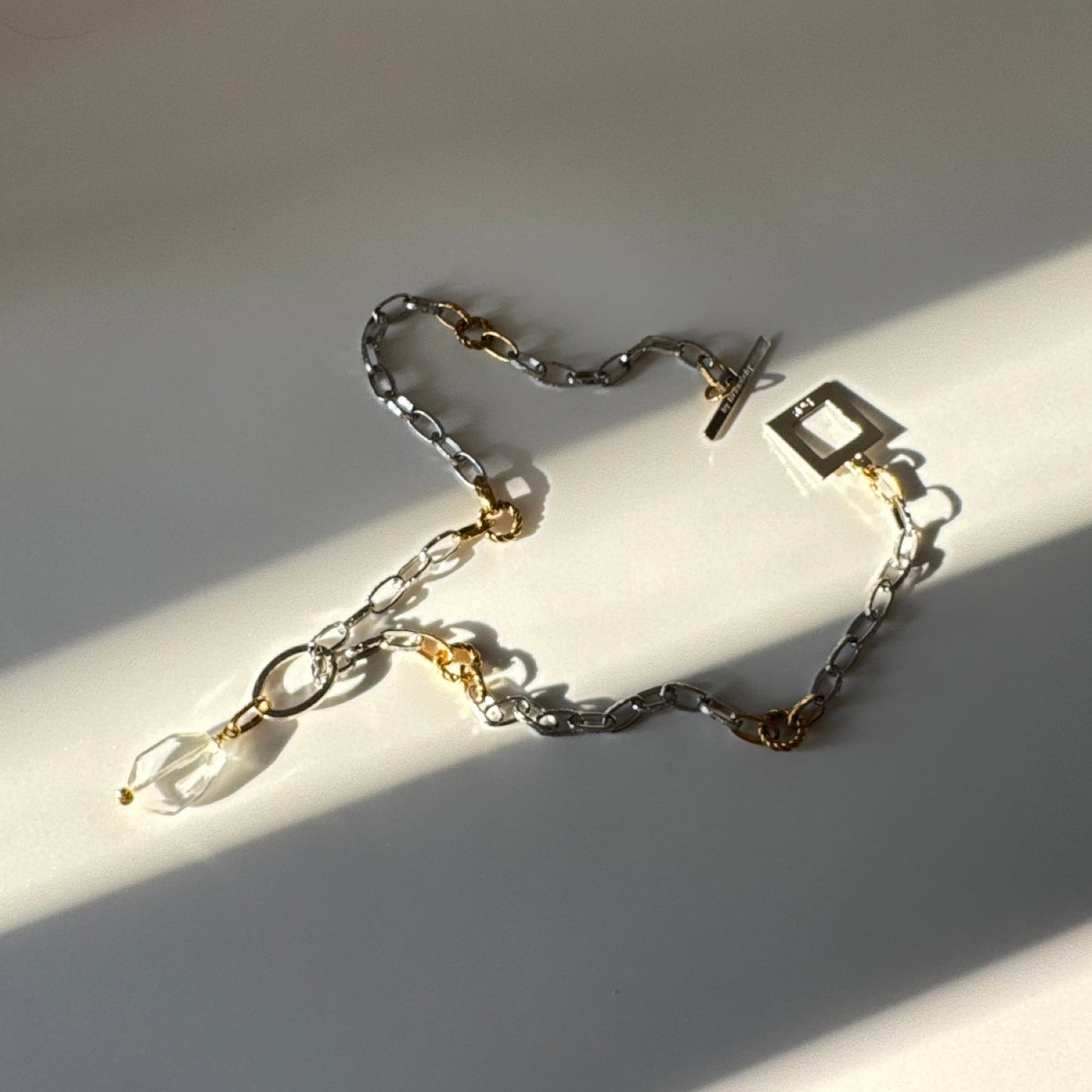 Elegant hänge med äkta bergkristall, fasade kanter och egendesignad cirkel i rostfritt stål med sterling silver-pläterade detaljer. Gulddetaljer i rostfritt stål med 18K guld PVD-beläggning. Handgjort av Design by Brandeby.