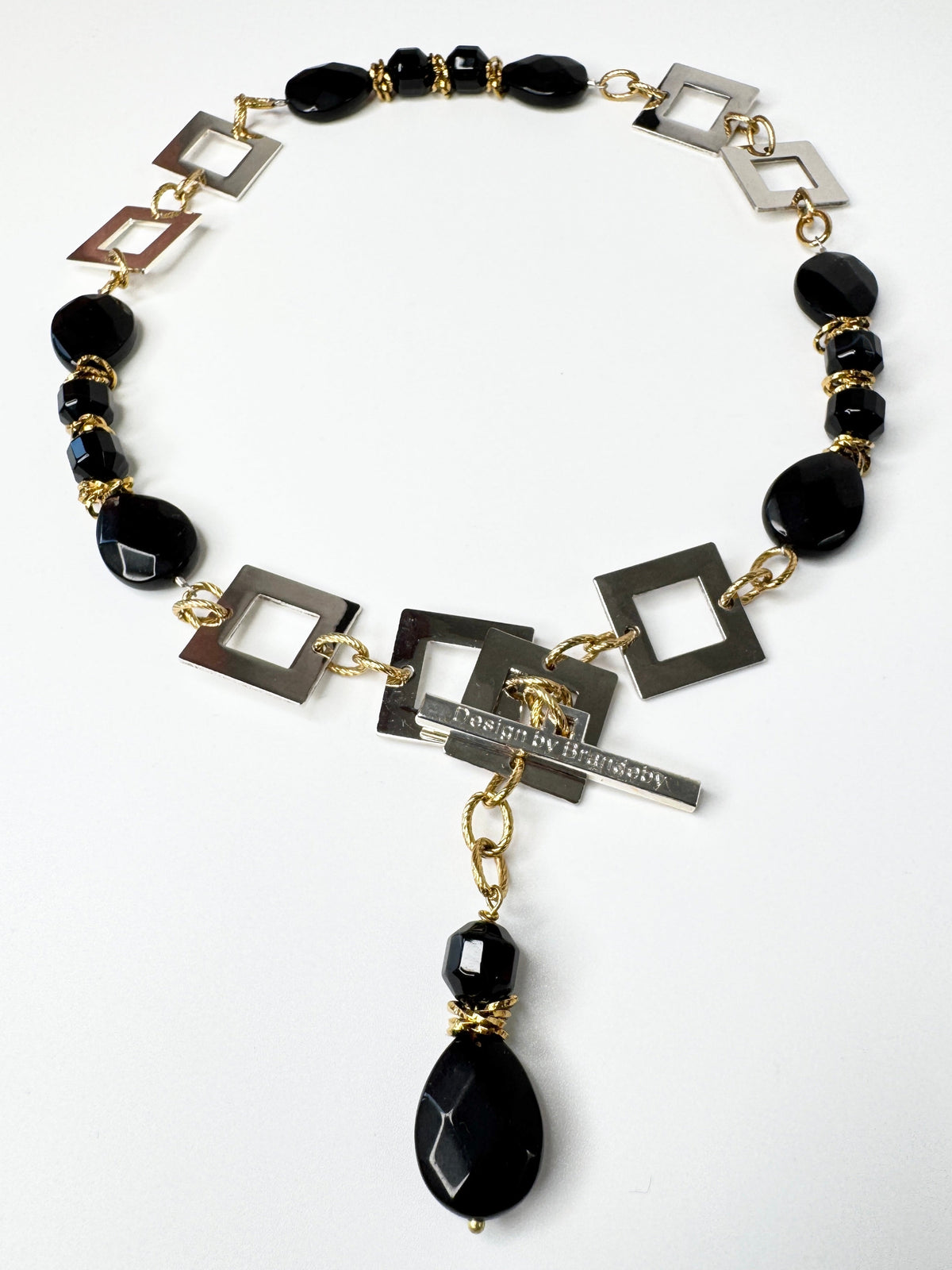 Kort halsband med fasettslipad svart onyx, egendesignade silverdetaljer och 18K guld PVD. Kan knäppas på två ställen. Handgjort av Sussie Brandeby i Helsingborg.